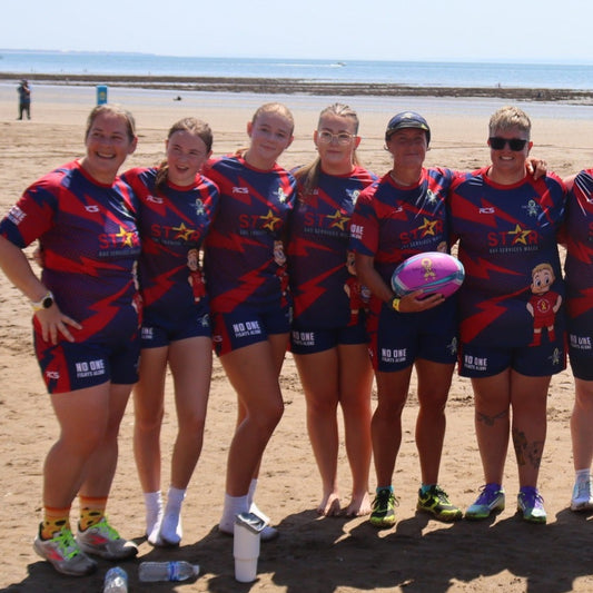 Group of people in sports uniforms posing on a beach with a clear sky.