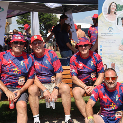 Group of people in matching sports jerseys sitting on a bench with promotional banners in the background.