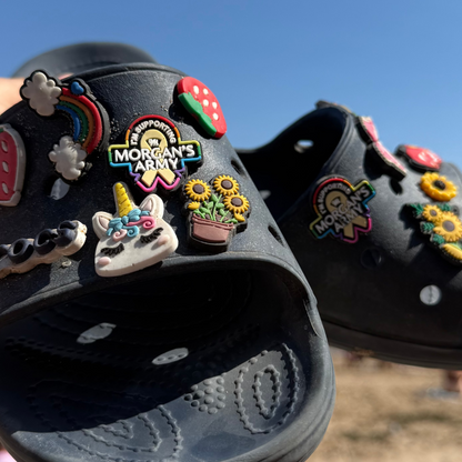 Black slides with colorful embellishments held by a hand on a beach.